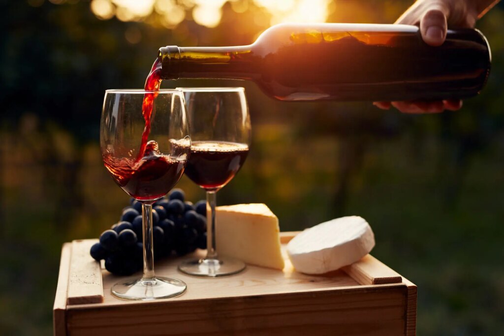 Red wine poured into two glasses beside cheese and grapes at sunset