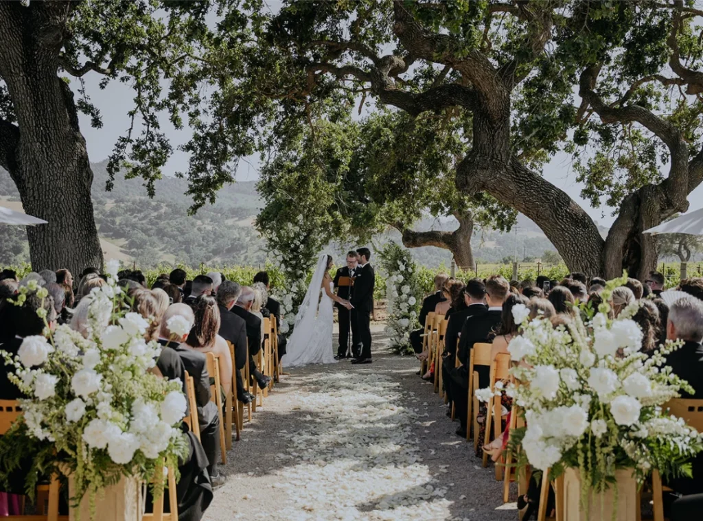 An outdoor ceremony under the oaks at Sunstone, guests seated along the aisle