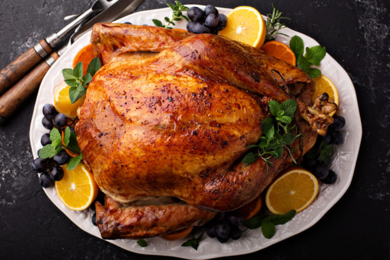 A roast turkey on a platter garnished with orange slices, grapes and herbs