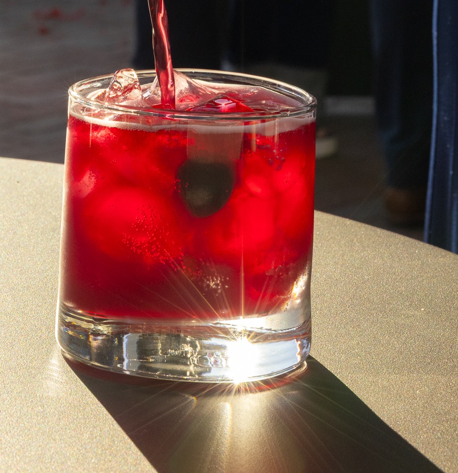 Deep red Sunstone Elixir serve poured over ice in a straight-sided tumbler, late afternoon light