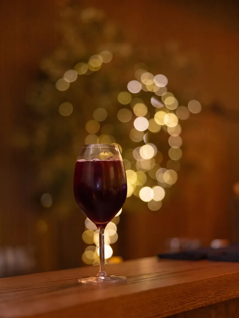 A stemmed glass of Sunstone Elixir on a wooden bar, warm lights blurred behind