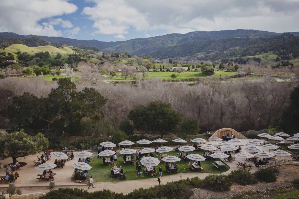 Guests at umbrella-shaded tables on the Sunstone lawn, with the Santa Ynez hills behind